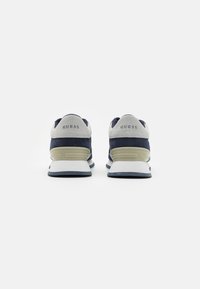 Sneaker blu navy con dettagli in suede grigio, suola bianca e logo "GUESS" sul tallone. Design leggero con superficie testurizzata.