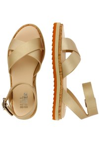 Sandalias beige con tiras cruzadas y suela de corcho y goma. Presentan un diseño plano con una correa ajustable en el tobillo y una plantilla texturizada.