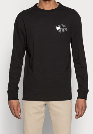 Schwarzes Langarmshirt mit weißem Logo auf der Brust. Mit gerippten Bündchen und Rundhalsausschnitt. Glattes Baumwollmaterial, reguläre Passform.