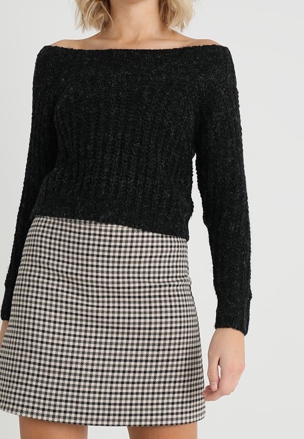 Schwarzer, schulterfreier Strickpullover mit strukturierter Oberfläche, kombiniert mit einem kurzen, karierten Rock im schwarz-weißen Hahnentritt-Muster.