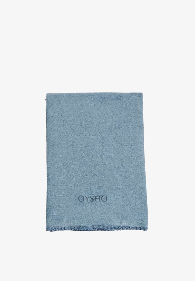 Platt blå mikrofiberhandduk, rektangulär form, mjuk textur, med en sydd kant och präglad "OYSHO"-logga i nedre hörnet.