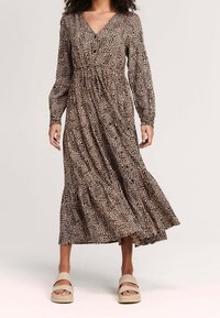 Leopardmönstrad maxikjol med långa ärmar, V-ringning och rynkad midja, med en utsvängd kjol. Bärs med ljusa sandaler.