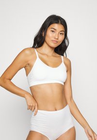 Vitt bralette med mjuka kupor, justerbara band och en slät yta. Kombineras med högmidjade vita trosor i ett liknande material.