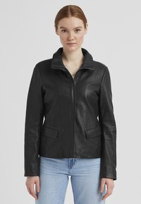 Schwarze Lederjacke mit Reißverschluss vorne, spitzem Kragen, zwei Fronttaschen und glatter Textur. Die taillierte Passform betont die Silhouette.