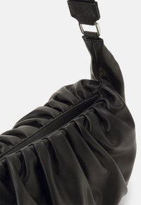 Sac en cuir noir froncé avec une texture lisse et une large bandoulière ornée d'une boucle métallique. Le design est à la fois souple et structuré.