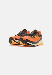 Zapatillas de trail running con una parte superior de malla naranja y negra, detalles texturizados, una suela acolchada y una suela exterior resistente para tracción.