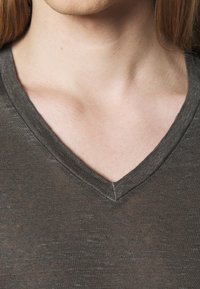 T-shirt grigio scuro a V con un tessuto morbido e texturizzato. Il collo presenta un dettaglio di cucitura pulito, sottolineando la semplicità della maglietta.
