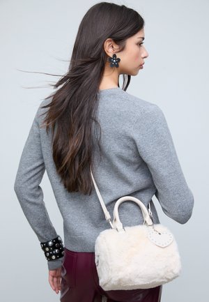 Maglione grigio con maniche lunghe, polsino nero con borchie e pantaloni color bordeaux. Borsa bianca in pelliccia sintetica con etichetta a forma di cuore e dettagli argentati.