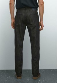 Dunkelblaue Jeans mit geradem Schnitt, ausgestattet mit zwei Gesäßtaschen und einer subtilen Textur. Tragen Sie braune Schuhe, von hinten gezeigt.