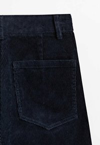 Pantalon en velours côtelé bleu foncé avec une poche arrière et une boucle de ceinture visibles sur un fond blanc uni.