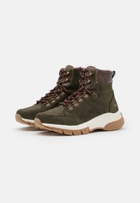 Botas de senderismo de ante verde con acentos marrones, presentando herrajes metálicos, cordones marrones, un cuello acolchado y una suela gruesa color crema.