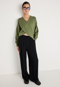 Ελαιόχρωμο πλεκτό μπλουζάκι με βαθύ V- λαιμόκοψη, συνδυασμένο με μαύρο παντελόνι ψηλής μέσης και φαρδιάς γραμμής. Λαμπερά μαύρα μοκασίνια ολοκληρώνουν την εμφάνιση.