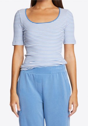 Mujer con una camiseta ajustada de rayas horizontales blancas y azul claro de manga corta y pantalones azul claro de talle alto.