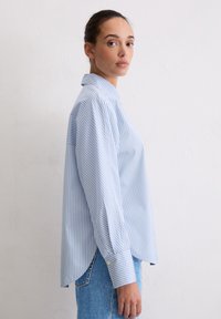 Blue and white striped button-up shirt with a collar, long sleeves, and a curved hem. Material appears lightweight and smooth.