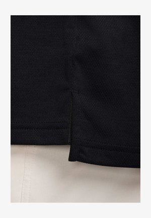Sort tekstil med en struktureret overflade, der har en side-split og kontrasterende syninger mod et lyst stof nedenunder.