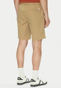 Pantaloni corti khaki con cintura elastica, tasca posteriore e taglio dritto, abbinati a calzini bianchi e sneaker in bianco e nero.