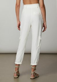 Pantalones cargo blancos con puños enrollados, que cuentan con bolsillos laterales y un ajuste relajado, fabricados con un tejido ligero. Llevados con sandalias de tiras.