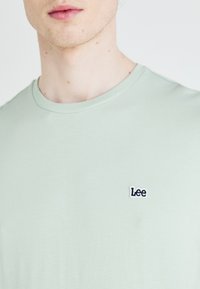 Camiseta de manga corta verde claro hecha de tejido suave, con un pequeño logotipo bordado de "Lee" en el lado izquierdo del pecho. Escote redondo.