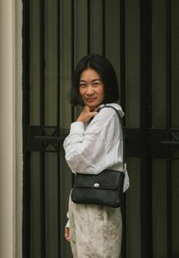 Sort læderhåndtaske med en struktureret overflade og en guldspænde, båret crossbody. Tasken har en rektangulær form og en tynd strop.