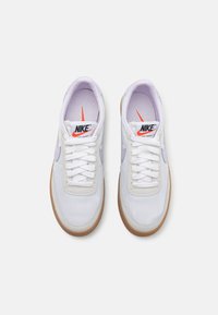 Adidași din plasă albă cu accente lila, vârful rotund, design texturat cu șireturi și talpă din cauciuc. Logo-ul Nike este prezent pe limbă.