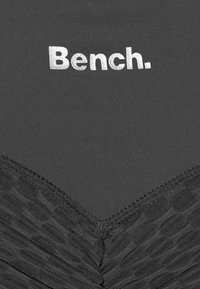 Musta vaate, jossa on tekstuuripohjainen alaosa geometrisella kuviolla ja sileä yläosa, jossa on hopealla sanat "Bench.".