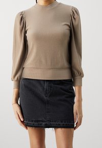 Top a costine marrone con maniche a palloncino e scollatura alta, abbinato a una gonna di jeans nera con orlo sfilacciato.