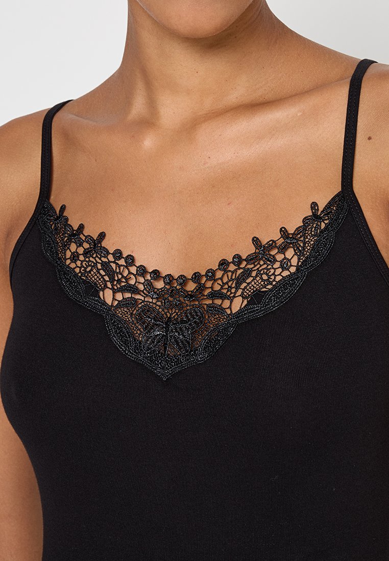 Schwarzes Top mit einem blumigen Spitzen-Ausschnitt mit aufwändigen Details und gewelltem Rand. Der Stoff ist glatt und eng anliegend.