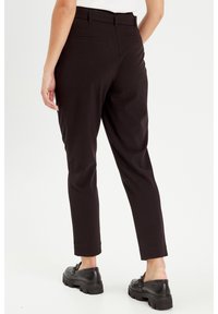 Schwarze Slim-Fit-Hosen mit glatter Textur, mittelhoher Taille, Gürtelschlaufen und Gesäßtaschen, kombiniert mit schwarzen klobigen Schuhen.