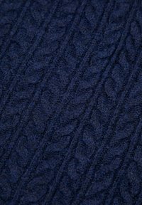 Granatowy dzianinowy materiał o fakturze warkocza, z wyraźnie podniesionymi kształtami liści. Miękki, wełnopodobny materiał, ukazujący misternie wykonane detale.