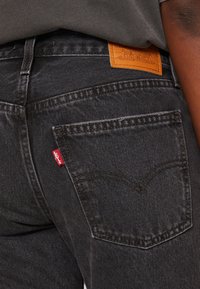 Acercamiento de unos vaqueros de denim gris oscuro con una etiqueta roja de Levi's en el bolsillo trasero y un parche de cuero marrón de la marca en la cinturilla.