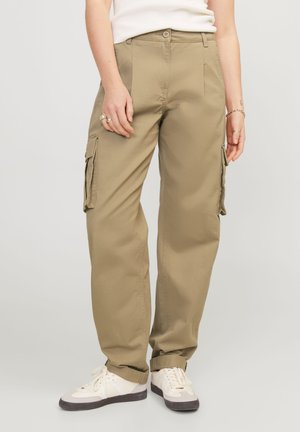Beige cargobroek met een losse pasvorm, voorzien van zijzakken en een eenvoudige knoopsluiting. G gedragen met witte sneakers en een strak T-shirt.
