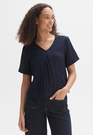 Navy blue short-sleeve blouse with a V-neck and pleat detail. Made of textured fabric, featuring rolled cuffs and a relaxed fit.