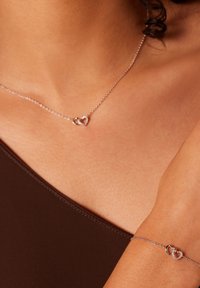 Zilveren ketting met twee verstrengelde hartbedels; bijpassende armband met een hartsluiting; fijne schakels; gladde textuur.