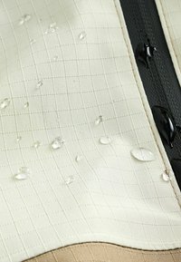 Gouttelettes d'eau claires sur un tissu texturé blanc et noir avec des coutures visibles et un motif en grille.