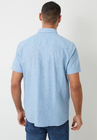 Camicetta azzurra chiara a maniche corte con colletto, realizzata in un tessuto texturizzato, con un design pulito sul retro e un orlo leggermente curvo.