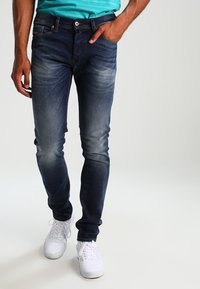 Mörkblå denimbyxor med slim fit, med blekta partier, fem fickor och blixtlås. Bärs med vita sneakers.