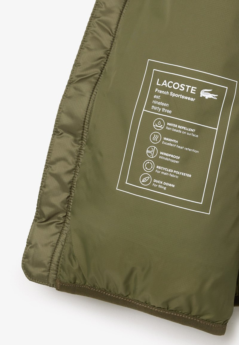 Chaqueta acolchada de color verde oliva con tejido repelente al agua y a prueba de viento, con una etiqueta que detalla los materiales: poliéster reciclado y plumón de pato.