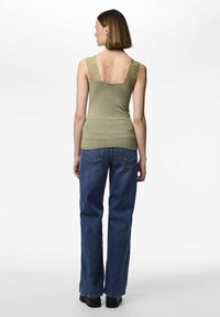 Olivengrønn tanktop med blondesnører, tettsittende design og myk tekstur, kombinert med løse blå denimjeans og svarte platåsko.