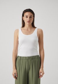 White cotton tank top with a scoop neckline, paired with loose-fitting, light green pants featuring an elastic waistband.