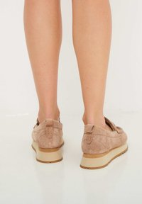 Zapatos de ante beige tipo slip-on con puntera redondeada, superficie texturizada y suela de goma de color claro, que cuentan con una pequeña lengüeta en la parte trasera y acentos de costura.