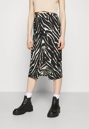 Kvinde iført nederdel med zebra-print, der går til knæene og har en slids foran, beige croppet top, hvide sokker og sorte ankelstøvler.