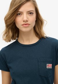 Navyblauwe katoenen t-shirt met een ronde halslijn, korte opgerolde mouwen en een klein geborduurd zakje met een vlagontwerp.