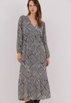 Abito a maniche lunghe con scollo a V in bianco e nero con motivo geometrico a diamante, vita arricciata e orlo a volant. Tessuto dalla texture liscia.