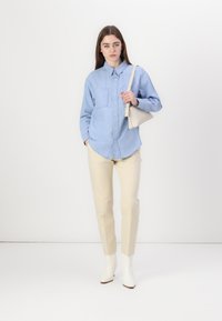 Gai zila džinsa kreklu ar pogām un divām krūšu kabatām, savienots ar bežām sašaurinātām biksēm un baltām potīšu zābakām. Minimalistisks rokas somiņa.