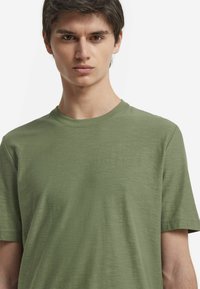 Olivgrön t-shirt i mjukt material, med regular fit, rund halsringning och korta ärmar med en jämn, lätt texturerad yta.