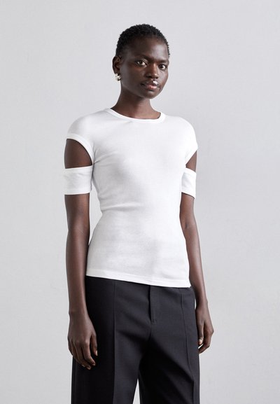T-shirt blanc à manches courtes avec des découpes aux épaules, fabriqué dans un matériau doux. Associé à un pantalon noir tailleur, au design ajusté.