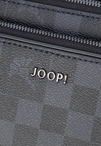 Szara portmonetka z wzorem i teksturowanym materiałem, z srebrnym logo "JOOP!" oraz gładkim zamkiem błyskawicznym wzdłuż górnej krawędzi.