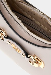 Borsa strutturata beige con hardware dorato e un accento di catena. Presenta una chiusura con zip e numerosi scomparti interni foderati in tessuto.