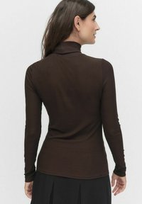 Brązowy prążkowany golf z długimi rękawami, dopasowany fason i gładka tekstura, noszony z czarną spódnicą, widok z tyłu.