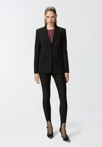 Crna odijelo s dvjema dugmadima, uparen s crnim tajicama i sjajnim crnim potpeticama. Prozirna bordo bluzica ispod sakoa s suptilnom teksturom.